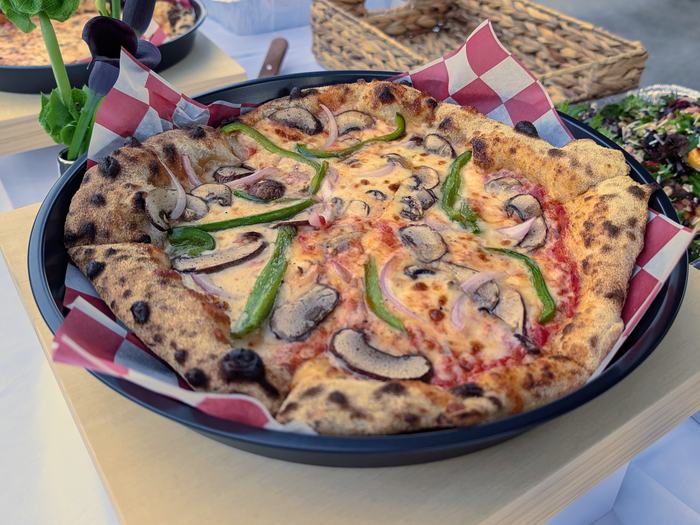 A pizza with mushrooms, green peppers and red onion on the buffet, its crust charred from the wood fire