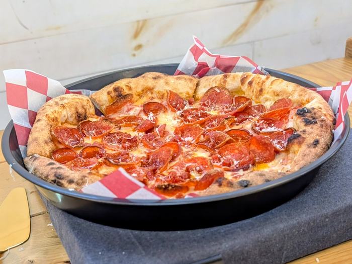 A Pepperoni Lovers pizza covered in cupped pepperoni, in a pan lined with red and white checked paper