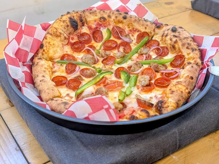 A Supreme pizza with cupped pepperoni, sausage, green peppers and red onion, in a pan on the buffet