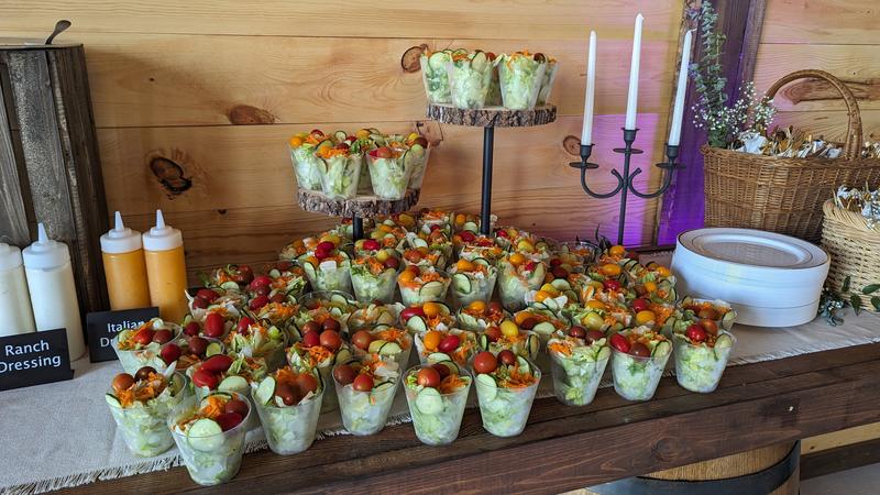 Individual salad cups on a tiered wooden stand at a catered event