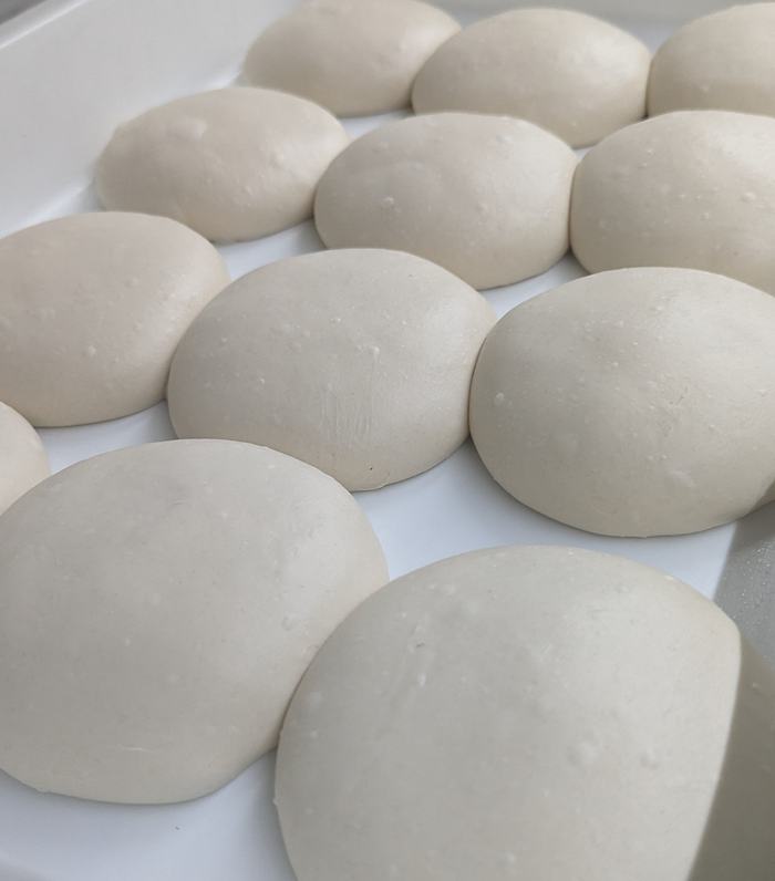Hand-balled dough proofing in a white tray, soft and spread