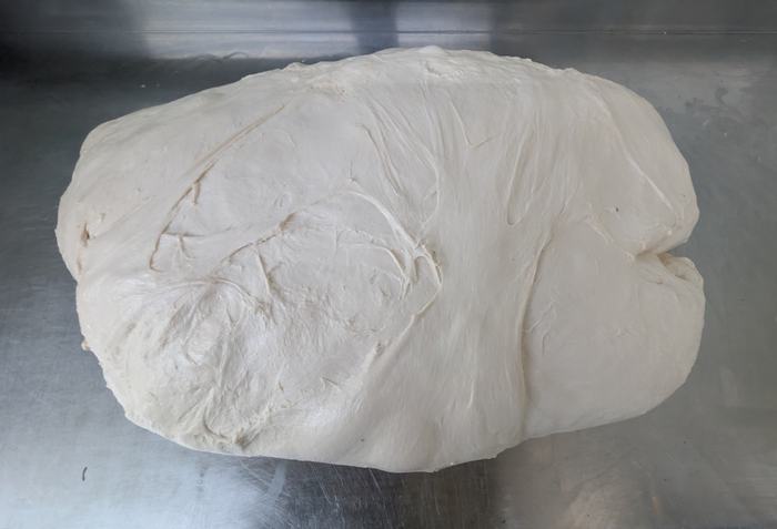 The whole batch of dough resting in one smooth mass on a steel table