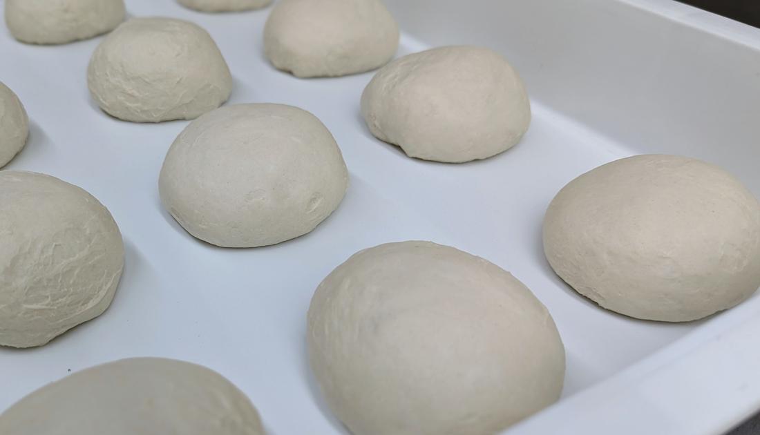 Hand-balled pizza dough proofing in a tray