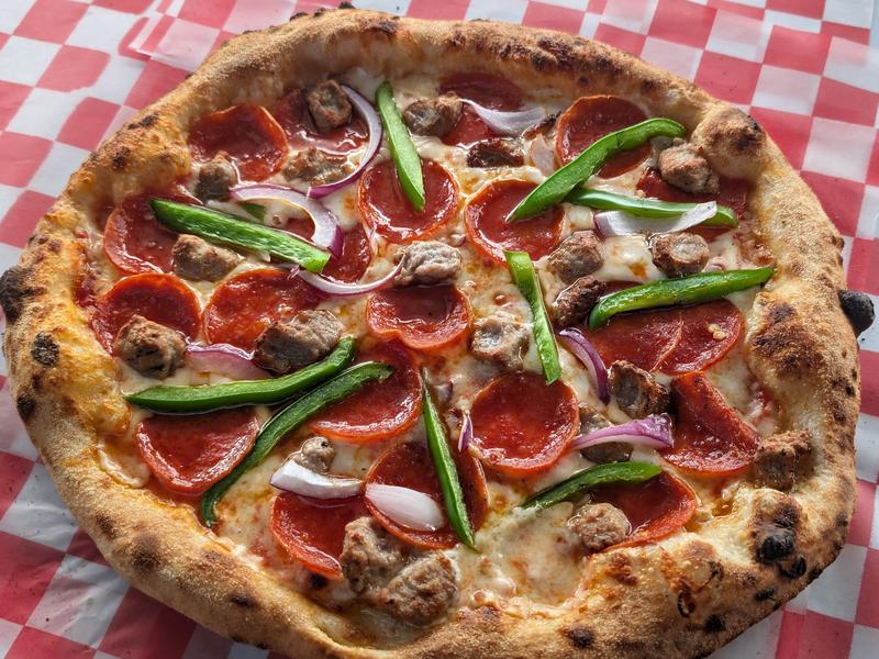 A pepperoni, sausage, pepper and onion pizza served on red check paper